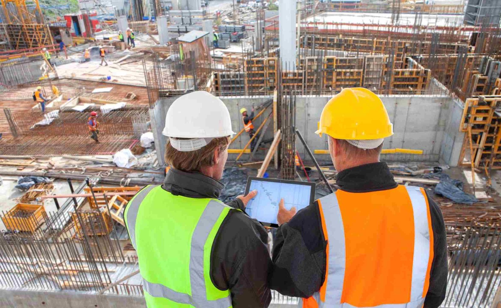 engineer architect with hard hat and safety vest working together in team on major construction site on computer tablet 